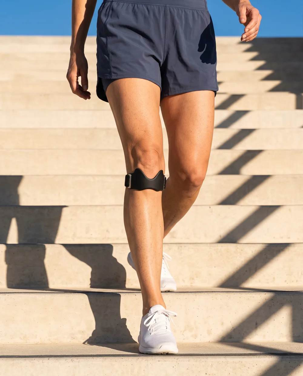 An adult wearing a compact black knee strap while walking on sunlit outdoor steps